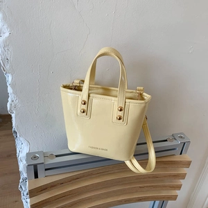 Elegant pale yellow patent leather bucket bag with gold rivets and shoulder strap