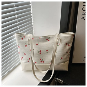 Cream corduroy tote bag with cherry prints and leather handles in a sunny setting