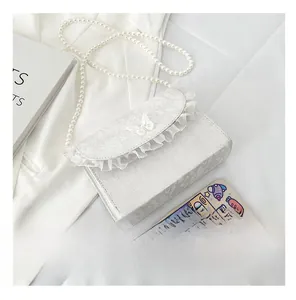 Close-up of white lace shoulder bag with bow detail and pearl strap shown next to a phone
