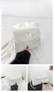 Detailed close-up of white lace crossbody bag with pearl chain and butterfly accents