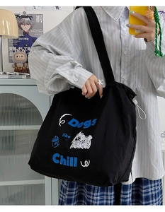 Detail shot of a black canvas tote bag featuring dog prints worn by a model in a casual setting