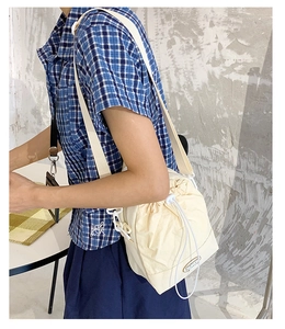 Detail of minimalist cream drawstring bucket bag with adjustable wide fabric strap