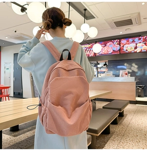 Detailed view of pink corduroy backpack with large front pocket and side drawstring pockets