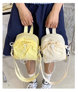 Close-up of drawstring crossbody bags in pale yellow and cream with fashion metal logo