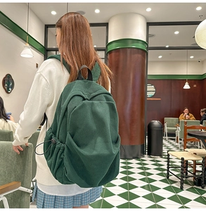 Detail of dark green corduroy backpack showing textured fabric and drawstring side pockets