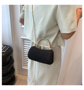 Model wearing a black glitter evening clutch with gold handle and chain strap on shoulder