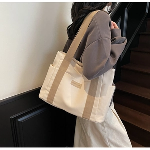 Dettaglio borsa tote in tela color crema con manici kaki e toppa in pelle di lusso