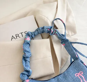 Detail of blue denim handbag featuring pink rose embroidery and ruffled handle design