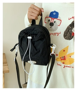 Detail of black nylon crossbody bag with white drawstrings and functional side hook