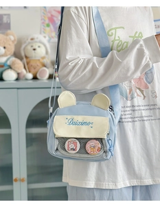 Close-up of light blue crossbody ita bag featuring clear pocket and cute bear badges