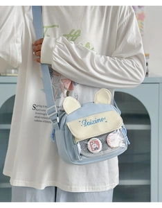 Close-up of light blue canvas crossbody bag with clear PVC pocket and cute badges