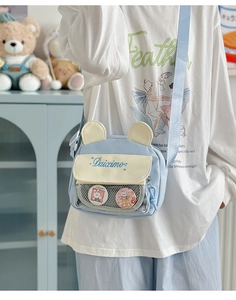 Detail of cute bear-eared crossbody bag with clear pocket worn by model in light blue