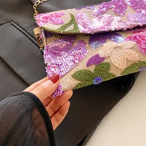 Macro-opname van fijn bloemig borduurwerk en lovertjes op een chique envelop clutch