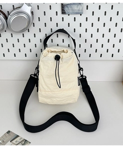 Detalle del bolso tipo saco de nailon crema con cordón negro y etiqueta de moda