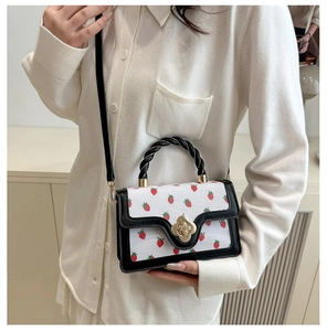 Detail of strawberry print crossbody bag featuring a woven handle and golden floral clasp