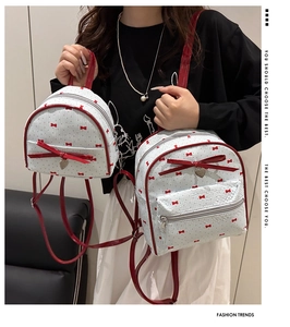 Detalle de mini mochila blanca con lazos rojos y colgante de corazón sostenida por modelo