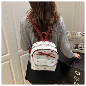 Mini mochila blanca con lazos rojos y tiras brillantes en la espalda del modelo