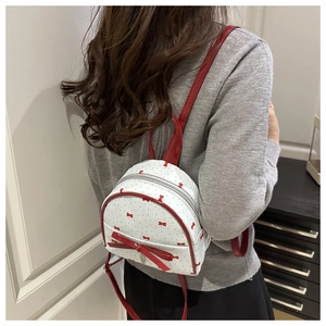 Vista detallada de una mini mochila blanca con lazos rojos usada por una modelo