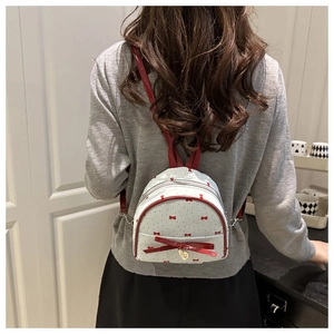 Detalle de mini mochila con patrones de lazo rojo y dije de corazón dorado en modelo