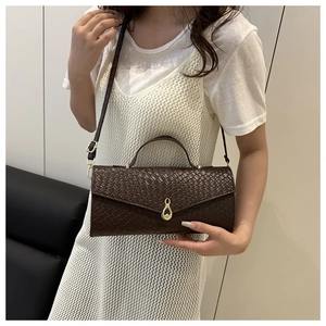 Dettaglio borsa a spalla marrone scuro intrecciata con fibbia dorata e texture in pelle