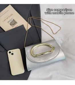 Mini silver clutch bag with gold handle and chain shown next to a phone for size comparison