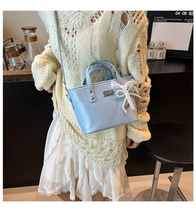 Détail du sac seau bleu clair avec nœud en dentelle et pendentif cœur en perle