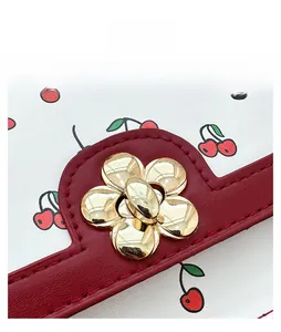 Close-up of golden petal twist lock on white leather bag with cherry prints and red trim