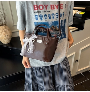 Détail d'un sac cabas marron brillant avec nœud en dentelle blanche et pendentif perle