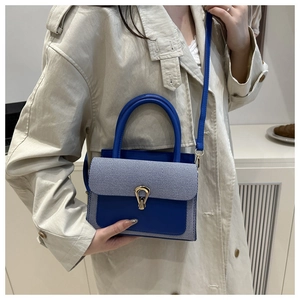 Detail of crossbody bag with blue leather, striped fabric, and gold horseshoe clasp