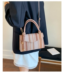 Detail of woven crossbody bag with striped pattern and gold ball decor on handle
