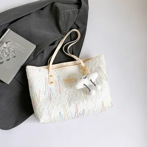 Close-up of quilted tote bag with wave embroidery and cute cloud plush charm accessory