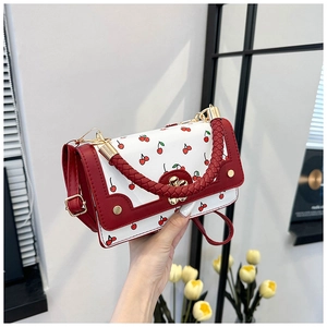 Detail of cherry print handbag featuring red woven handle and golden floral clasp
