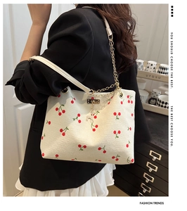 Detalle del bolso tote de pana blanca con estampados de cerezas y colgante de ciervo dorado