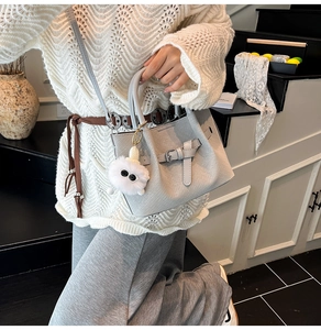 Detail of light grey woven texture handbag with crossbody strap and fluffy charm