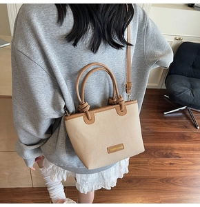 Detail of straw woven bucket bag with brown leather handles and knotted rope design