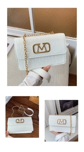 Detalle de bolso bandolera blanco con textura de cocodrilo, hebilla dorada en M y cadena