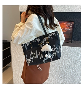 Detail view of black textured tote bag with contrast stitching and cloud charm accessory