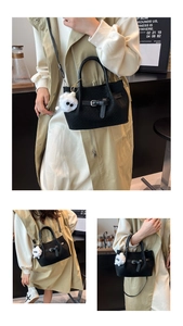 Detail of black pleated bucket bag with woven texture and a white plush charm