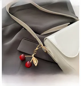Detail of red cherry bag charm with golden leaf on a white glossy leather shoulder bag