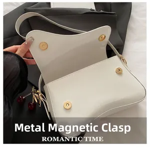 Detail of white saddle bag with metal magnetic buckles and cherry charm accessory