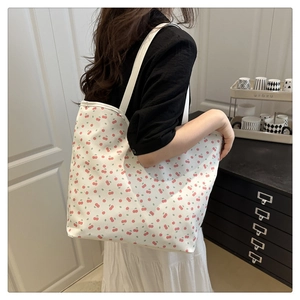 Detail view of canvas tote bag with red cherry print worn as an underarm shoulder bag