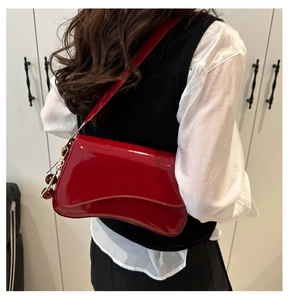 Model wearing a red patent leather underarm bag with a cherry charm and glossy finish