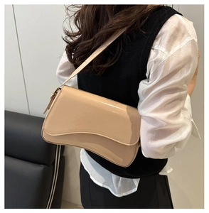 Chic beige patent leather underarm bag with a unique wavy flap shown in use
