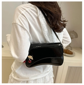 Detail of glossy black patent leather shoulder bag with cherry charm on white shirt