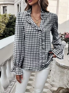 Detail of gingham blouse featuring elegant ruffled collar and buttoned cuffs in sunlight