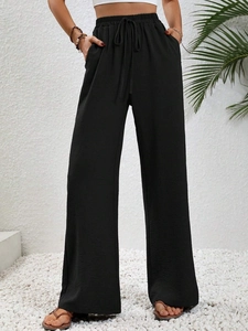 Dettaglio di pantaloni neri a gamba larga con coulisse elastica e tessuto con trama a pieghe