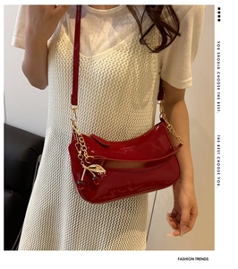 Detail of red patent leather shoulder bag with gold chain and cherry charm accessory