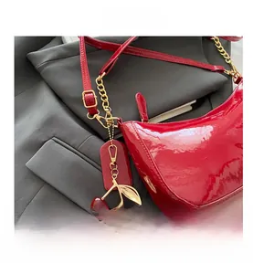 Detail of red patent leather hobo bag featuring golden chain and cherry charm accessory