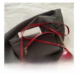 Close-up of red patent leather shoulder bag with gold metal buckle and chain details