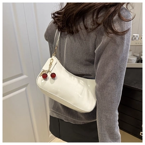 Detail view of white patent leather hobo bag with stylish red cherry bag charm on strap